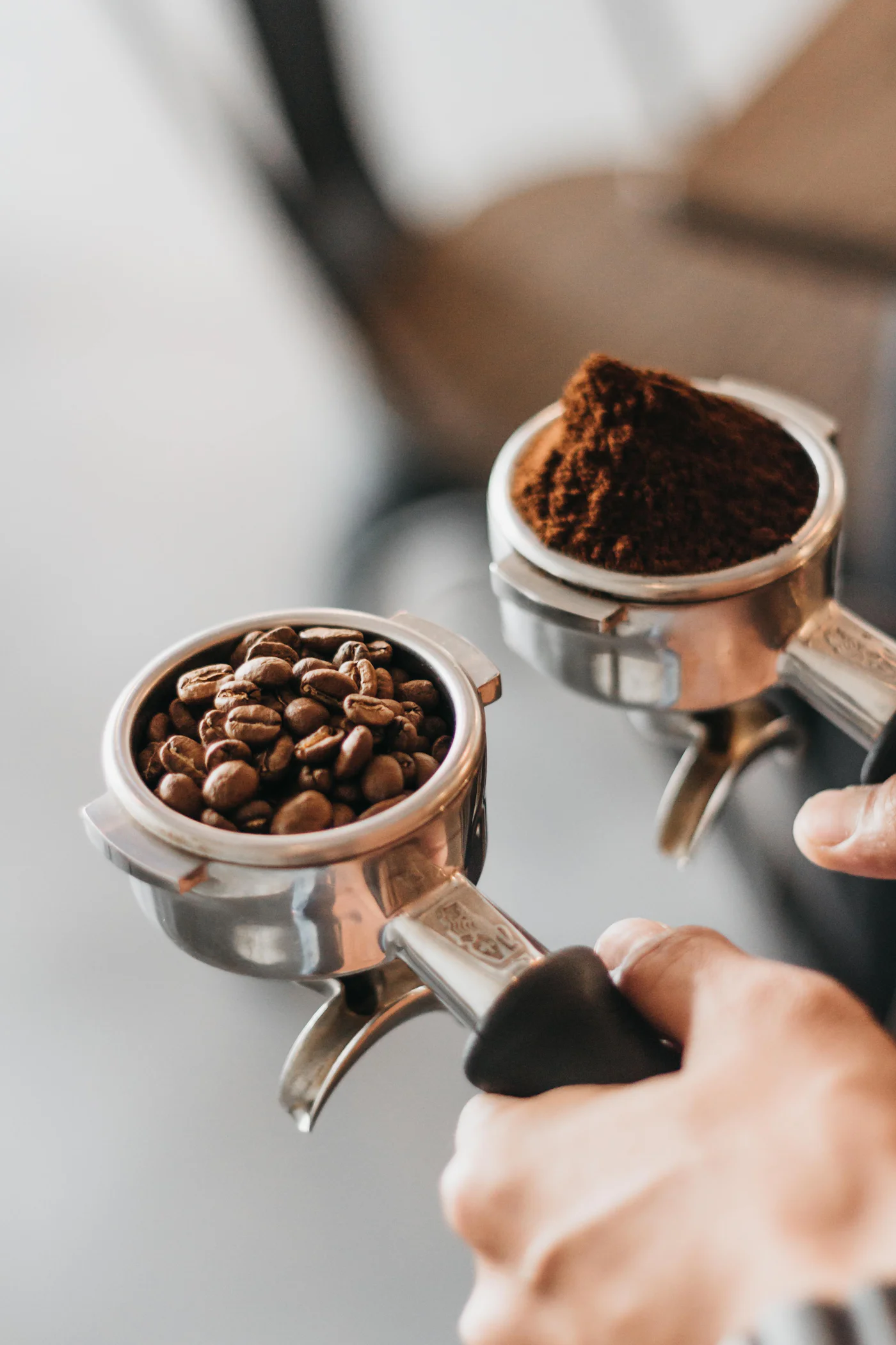 Barista ținând două portafiltre, unul cu boabe și unul cu cafea măcinată